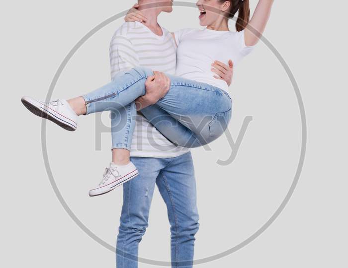 Man Holding Girl In His Arms. Couple Standing Isolated. Lovely Couple Looking At Each Other Girl Is Happy And Holding Hand Up. Young Couple, Family, Lovers Concept