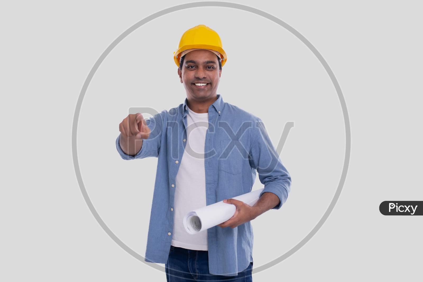 Construction Worker Holding House Plan In Hands Pointing In Camera. Architect Holding Blueprints. Yellow Hard Helmet.