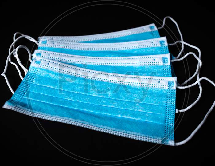 Four Surgical Face Masks Lying On Top Of Each In Black Background