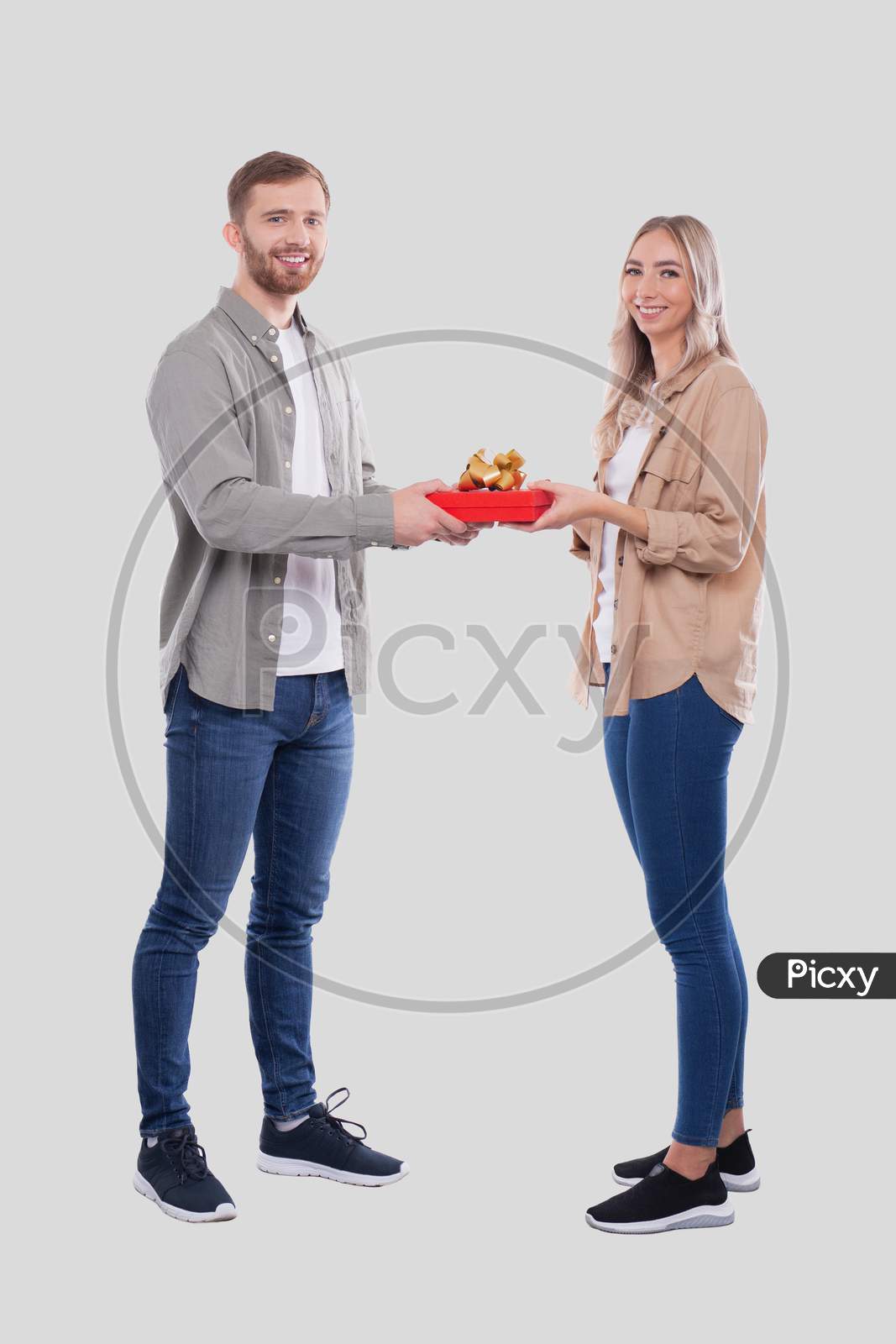 Couple Standing Looking Into Camera Holding Gift Isolated. Woman Suprised By Gift From Man. Man Making A Gift To Girl. Couple Day. Present For Girl