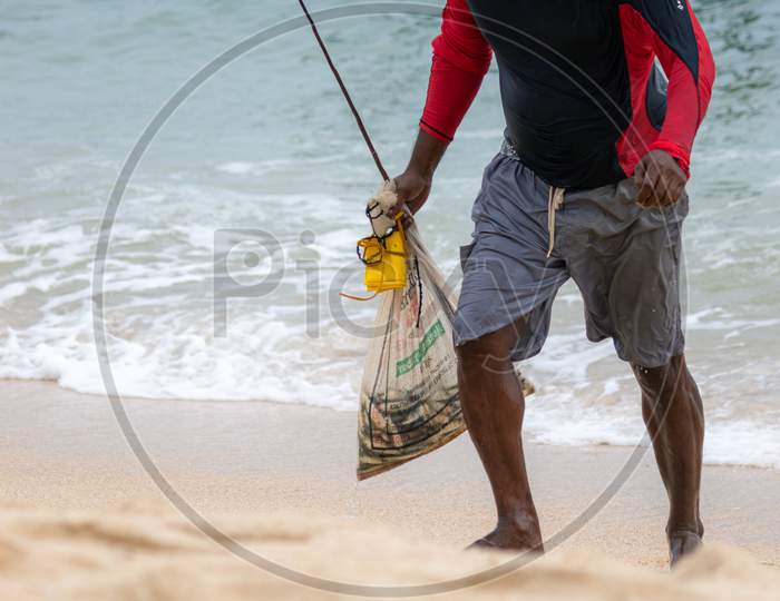 Fishermen Walking On The Beach With A Bag Full Of Fish With Head Down After Stilt Fishing For Hours.