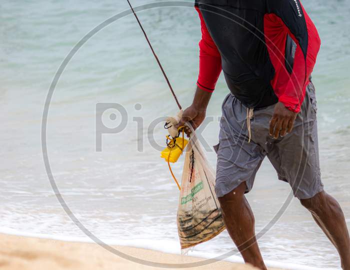 Fishermen Walking On The Beach With A Bag Full Of Fish With Head Down After Stilt Fishing For Hours.
