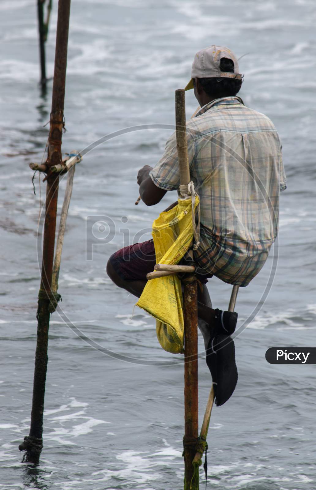 Image of Stilt Fisherman With His Wooden Rod Facing Back To The Camera With  His Yellow Pocket On The Pole, Fishing In A Traditional Unique Method In  Sri Lankan Culture, Sunny Bright