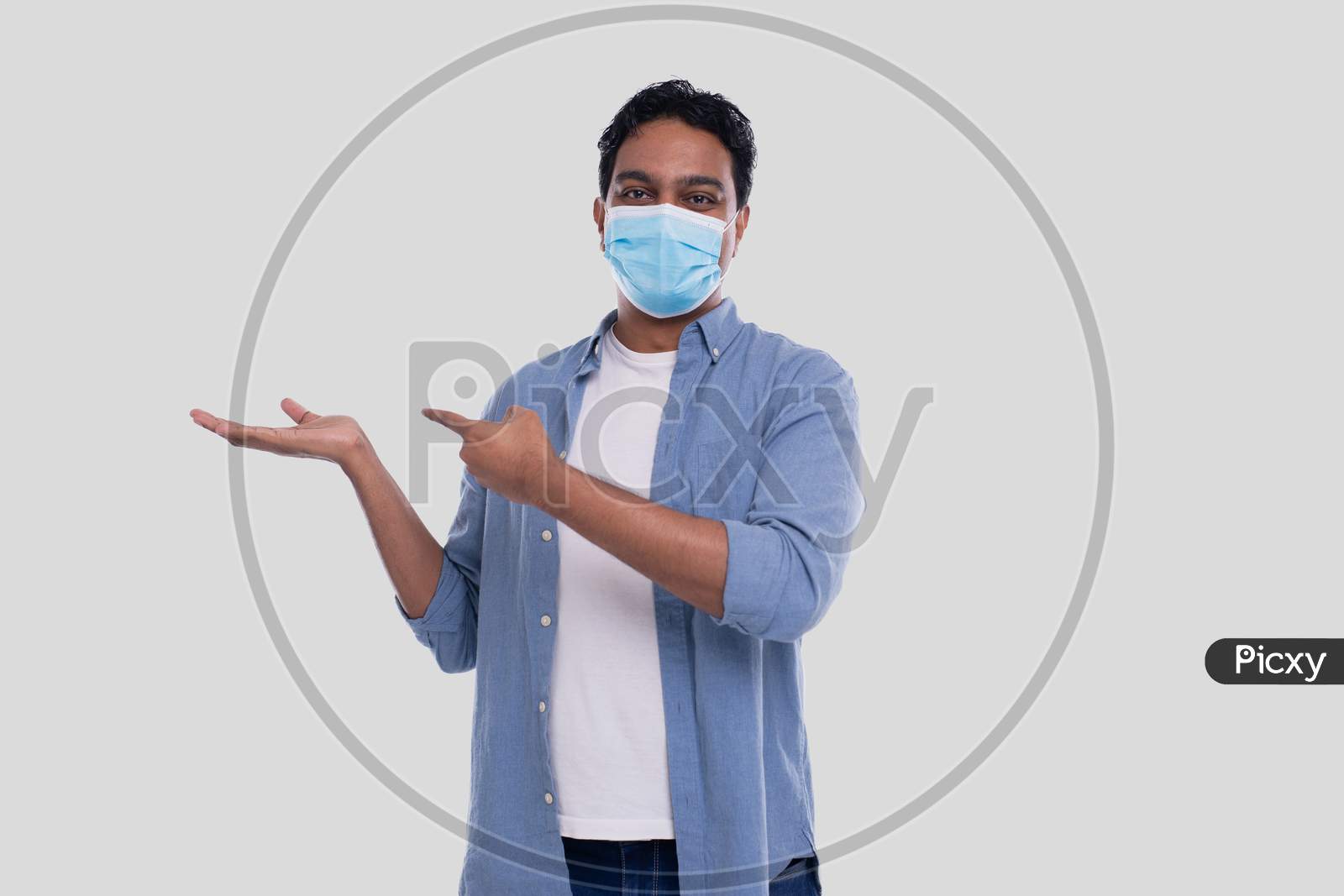 Man Showing Hand To Side And Pointing At It Wearing Medical Mask Isolated. Indian Man Wearing Medical Mask