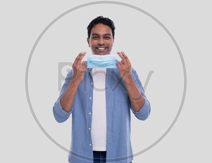 Indian Man Puts On Medical Mask Isolated. Man In Blue Shirt Showing How To Put On Medical Mask. Health, Virus, Medical Concept