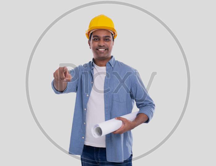 Construction Worker Holding House Plan In Hands Pointing In Camera. Architect Holding Blueprints. Yellow Hard Helmet.