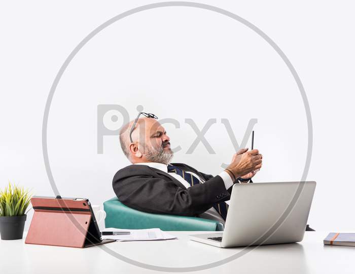 Mature Asian Indian Businessman Relaxing Or Resting In Armchair With Legs Up On Office Desk