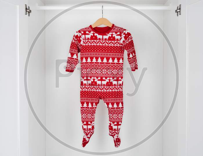 White And Red Christmas Pajamas Hanging On A Wooden Hanger In The Middle Of A White Closet.