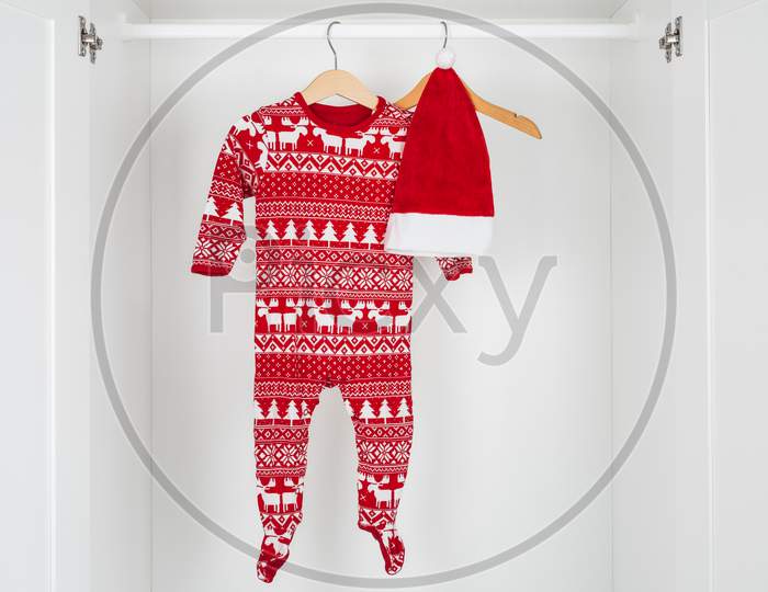 White And Red Christmas Hat And Pajamas Hanged On A Wooden Hangers In The Middle Of A White Closet.