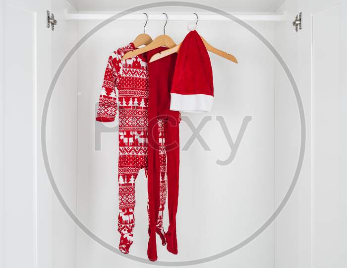 White And Red Christmas Pajamas, Hat And Tights Hanging On A Wooden Hangers In The Middle Of A White Closet.