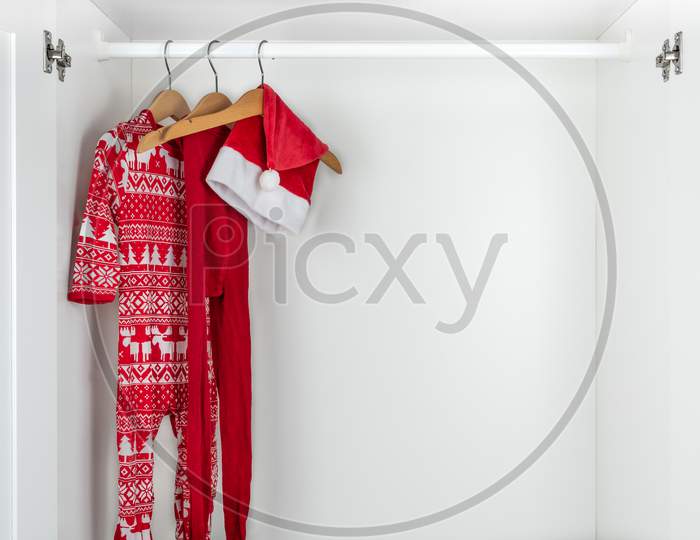 White And Red Christmas Pajamas, Hat And Tights Hanging On A Wooden Hangers On The Left Of A White Closet.