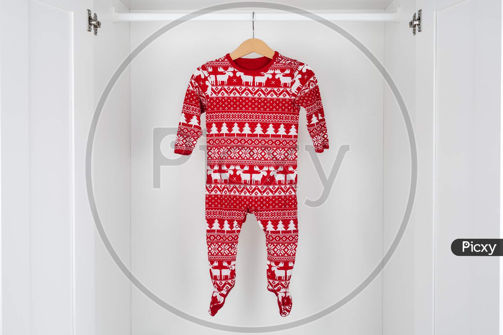 White And Red Christmas Pajamas Hanging On A Wooden Hanger In The Middle Of A White Closet.