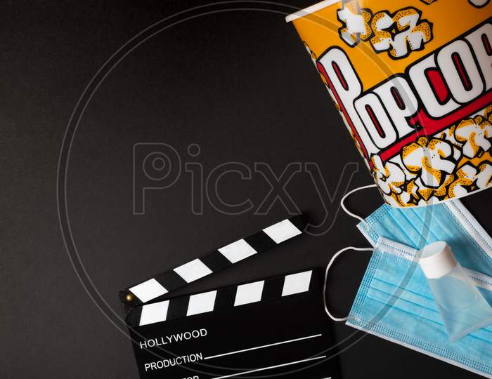 Movie Clapperboard, Hydrogel, Face Mask, And Popcorn Box On A Black Background During The Second Wave Of The Coronavirus Pandemic. Covid Concept.