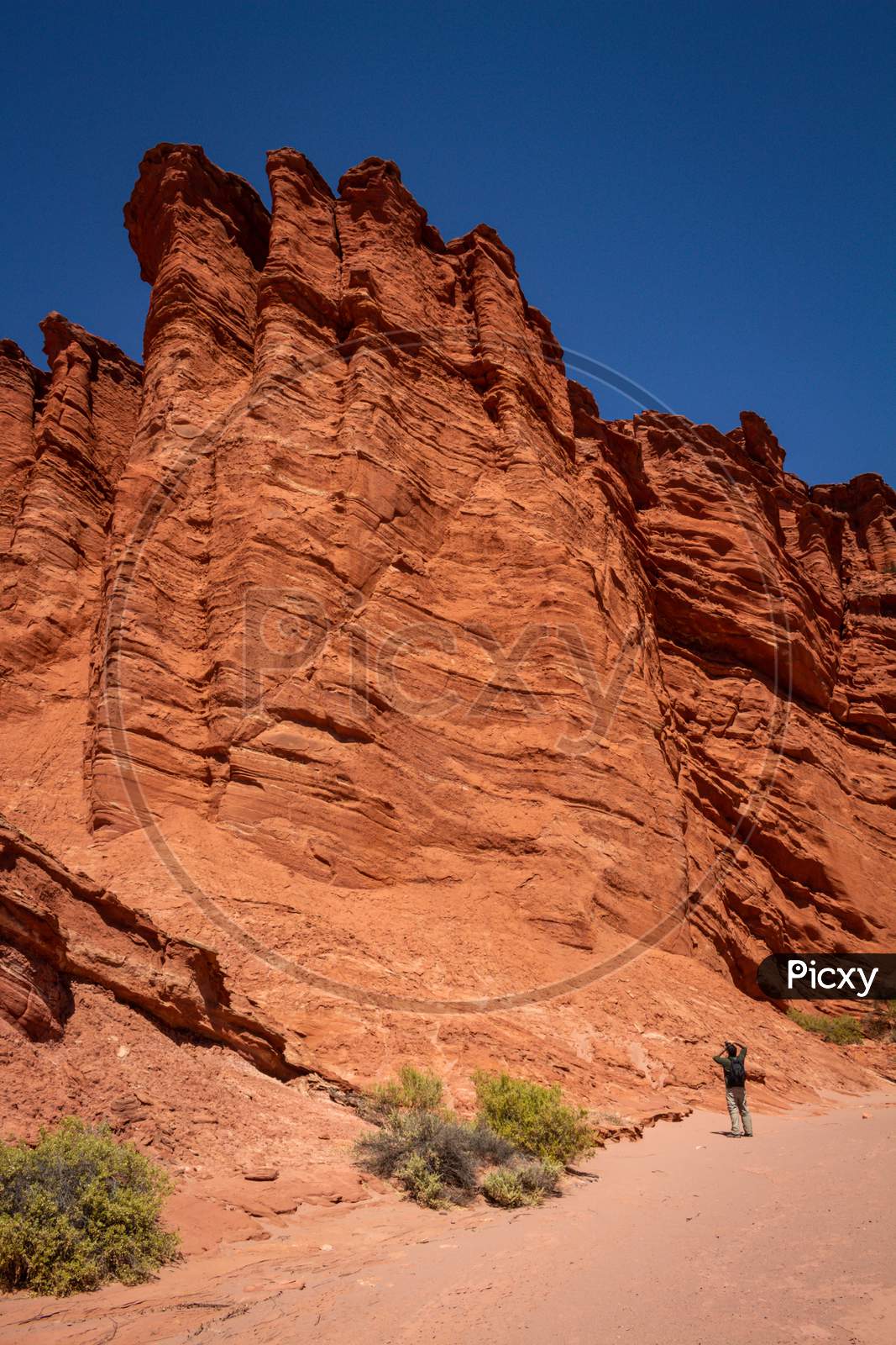 Backpacker Man Taking Photos Of The Geological Formations In The Talampaya National Park In The Argentine Republic. Reddish Rocks