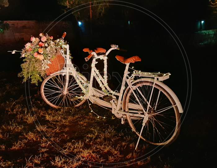 Old and decorative bicycle in black background. White decorative bicycle with garlands.