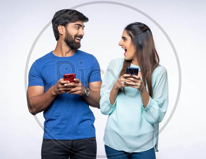 Indian Couple make happy gestures as they use Mobile Phones