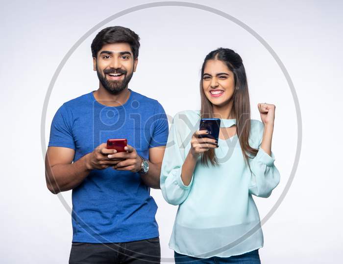 Young Indian Couple make happy gestures as they use Mobile Phones