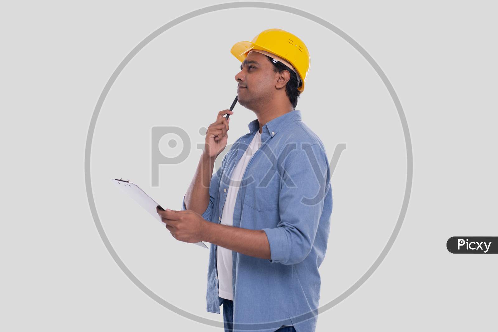Construction Worker Holding Clipboard In Hands Watching Up. Man Thinking. Architect Holding Blueprints. Yellow Hard Helmet.