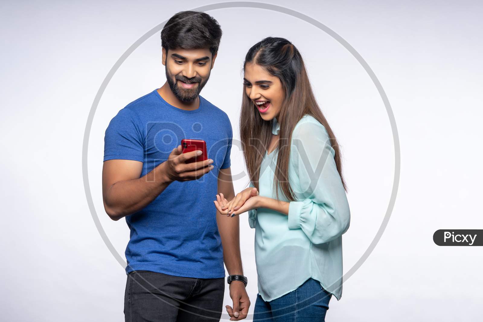 Happy Young Indian Couple making gestures while using a Smartphone.