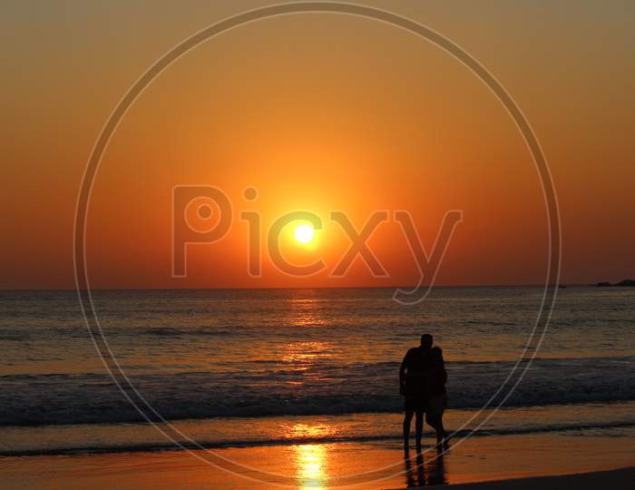A couple on a beach watching sunset golden hour silhouette romantic romance love