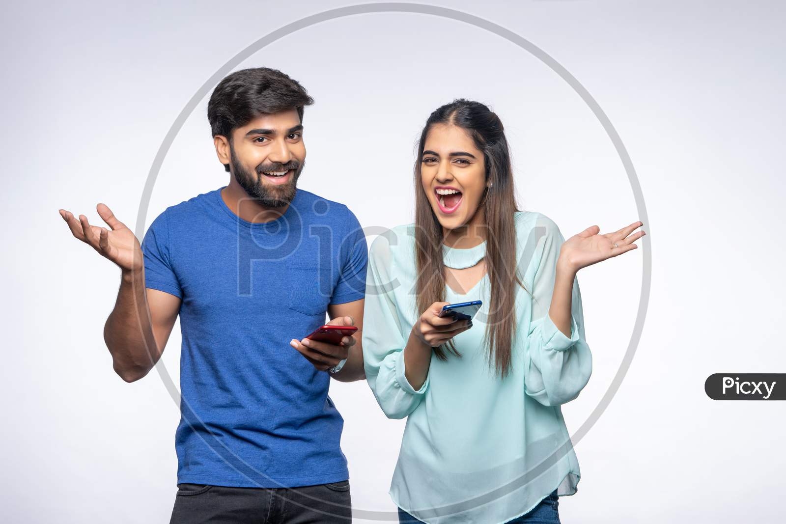 Young Indian Couple make happy gestures as they use Mobile Phones