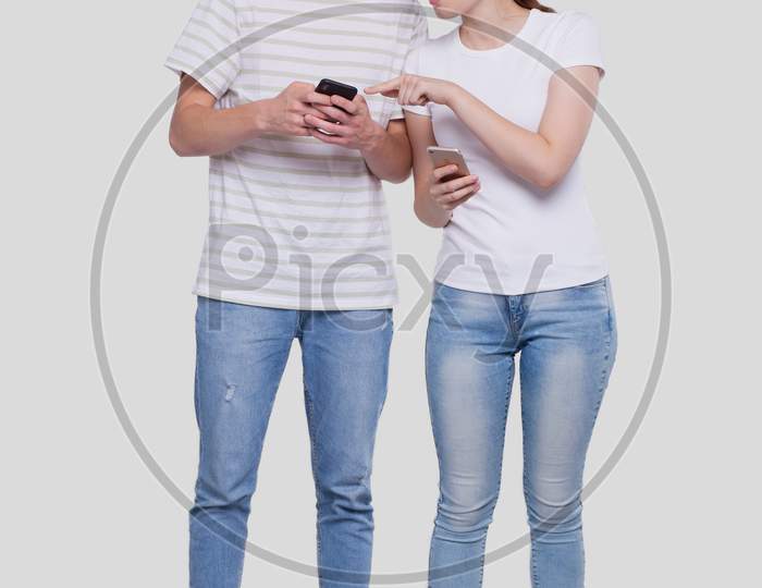 Couple Chatting On Phone. Couple Using Phones Standing Isolated. Couple Shopping Online. Girl Watching In Man Phone Surprised.
