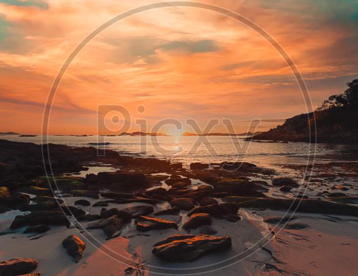 Horizontal Image Of A Tide On The Beach Over The Sand During A Colorful Sunset With The Islands As The Background And Copy Space