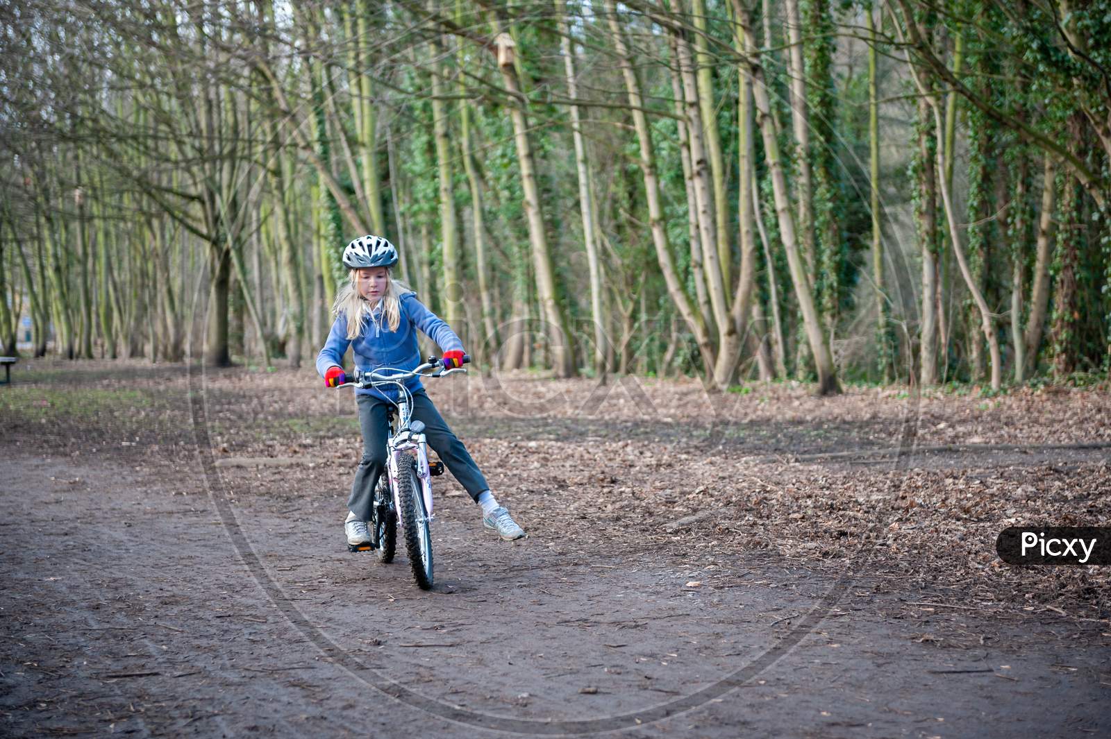 A Young Girl Balances While Riding A Bike Along A Country Track.