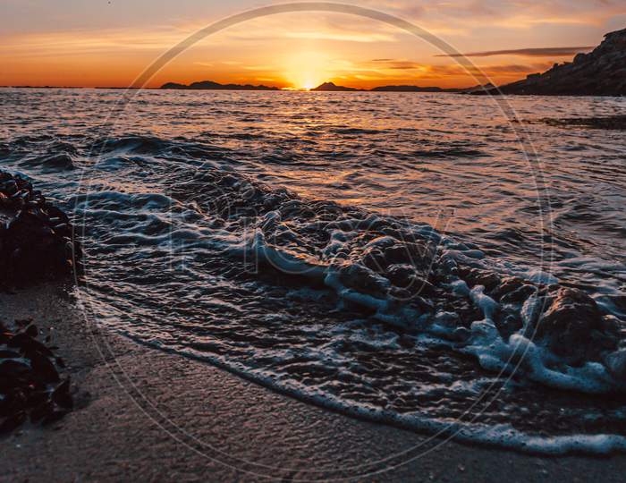Vertical Image Of A Tide On The Beach Over The Sand During A Colorful Sunset With The Islands As The Background And Copy Space
