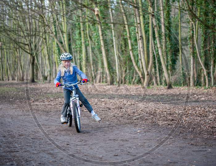 A Young Girl Balances While Riding A Bike Along A Country Track.