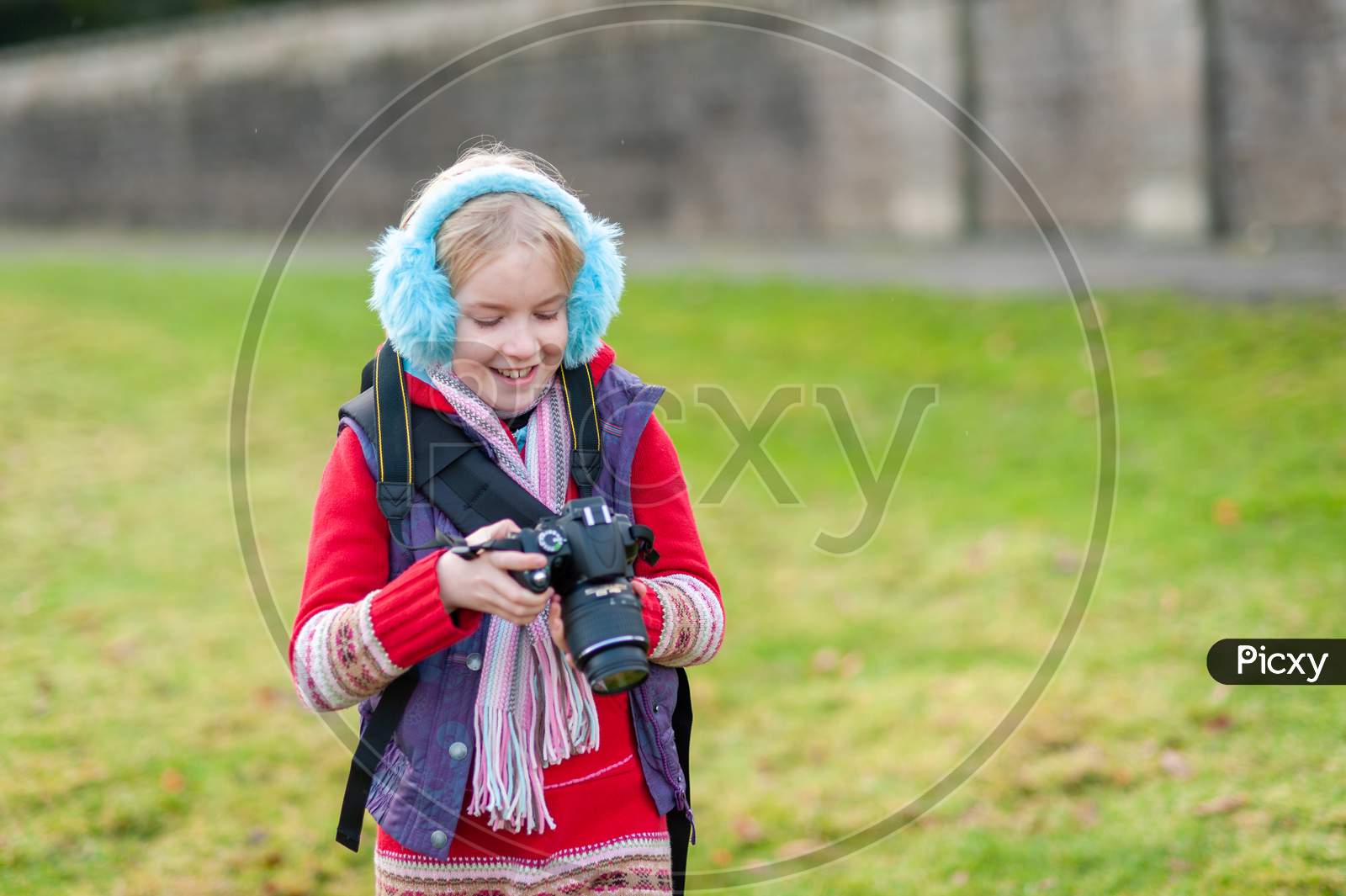 Happy Young Girl Holding A Camera And Wearing Blue Ear Muffs