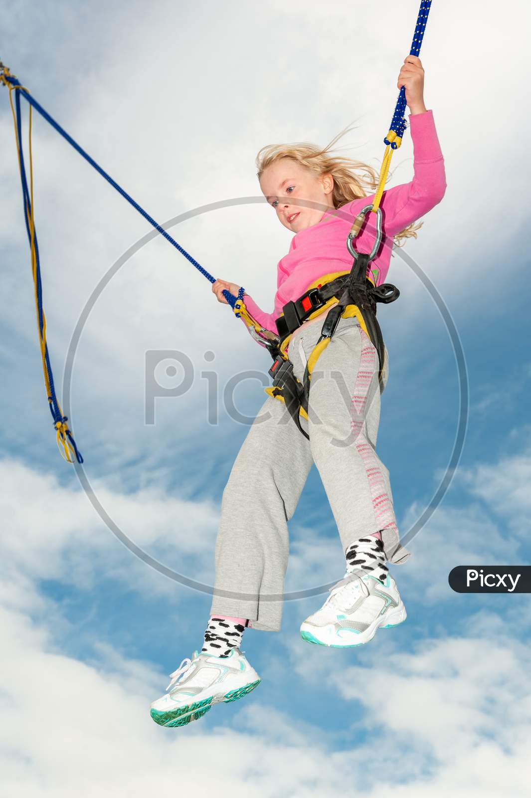 Happy Young Blonde Girl Bouncing While Attached To Bungee Cords
