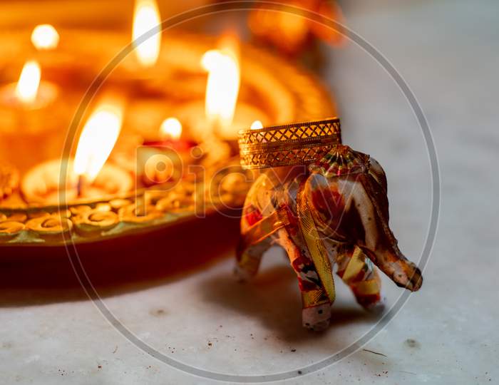 Elephant Incense Holder With Smoke Coming Out Of It And Beautiful Gold Painted Earthenware Diya Lamps Filled With Oil And Lit With A Flame In The Background