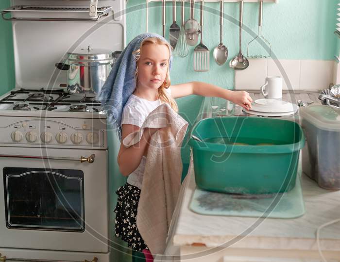 Young Girl Drying Dishes At A Kitchen Sink