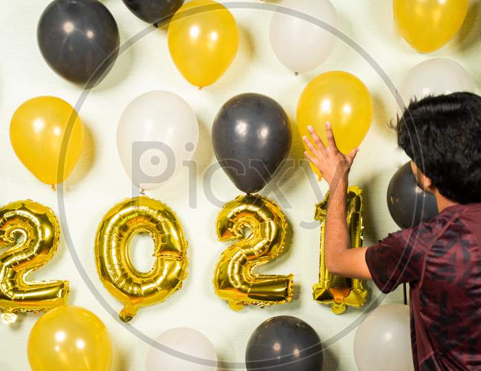 Concept Of 2021 New Year Party Decoration - Young Man Busy In Decorating Wall With Balloons For New Year Party Celebration.