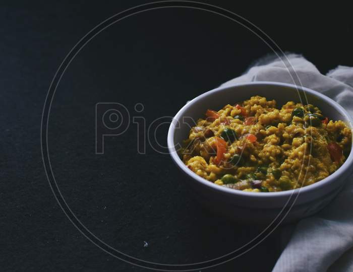 Indian style oatmeal porridge bowl with mixed vegetables on black background
