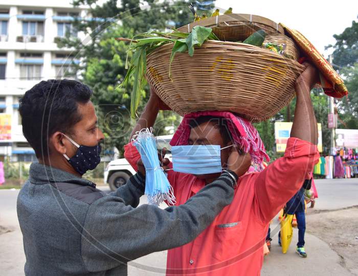 A member of puja committee help a devotee  to wear a mask on the occasion of Chhath Puja in Nagaon district, in the northeastern state of Assam on Nov 20,2020.