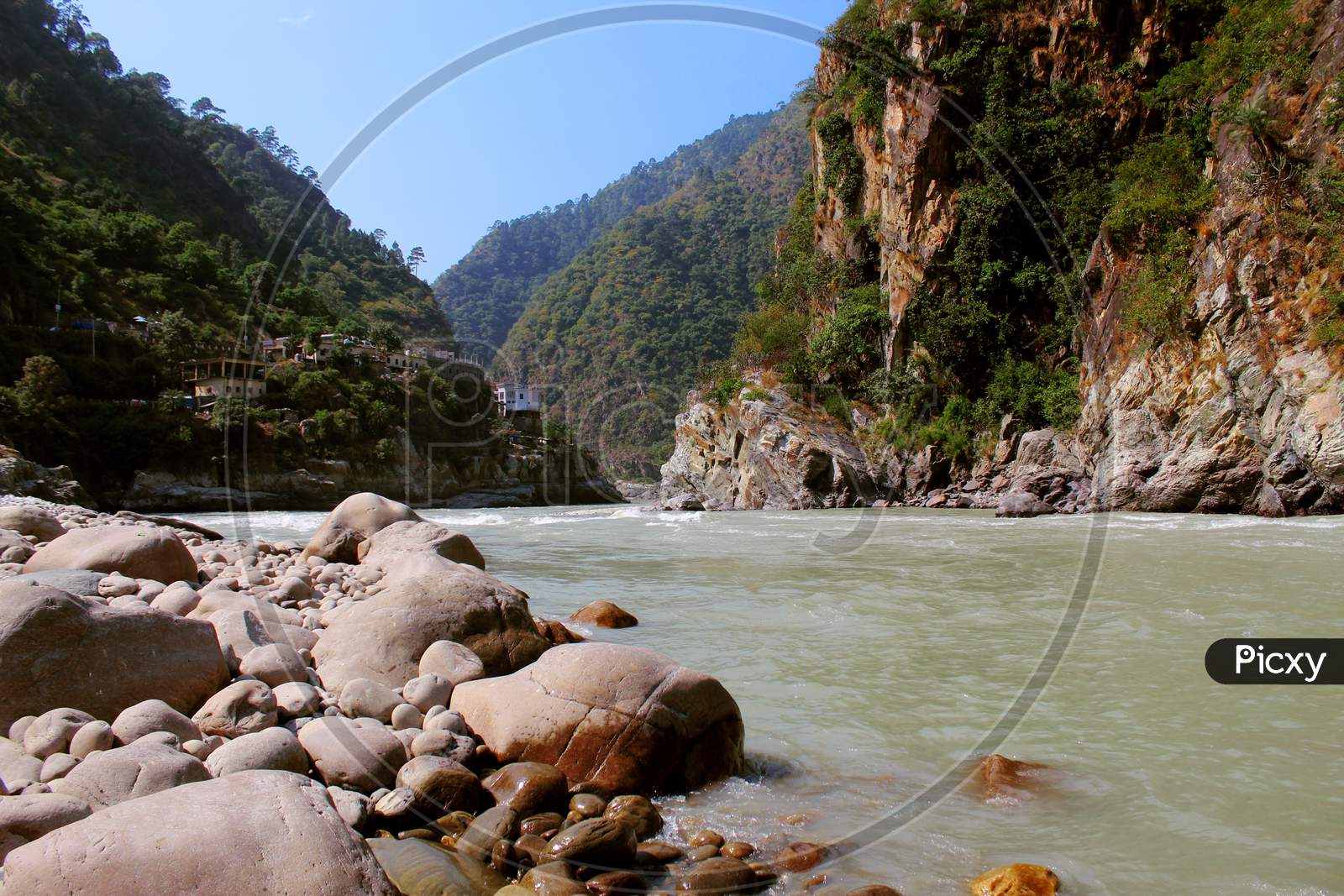 Landscape with mountains, forest and pines, river and blue sky & stones on riverside.