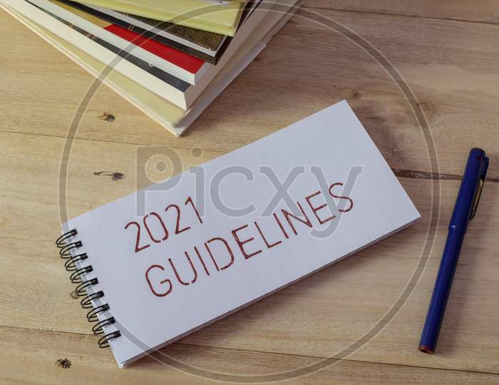 2021 GUIDELINES handwritten in notepad on wooden desk with pen and books.