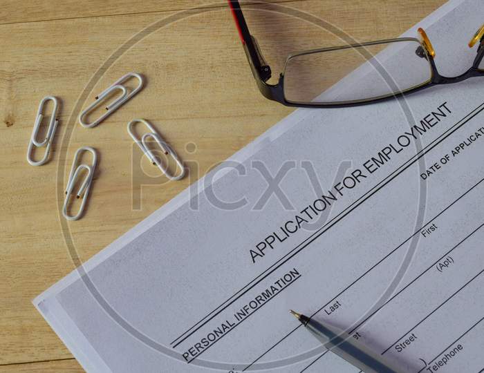 Application for Employment form on wooden desk with pen, spectacle and paper clips.
