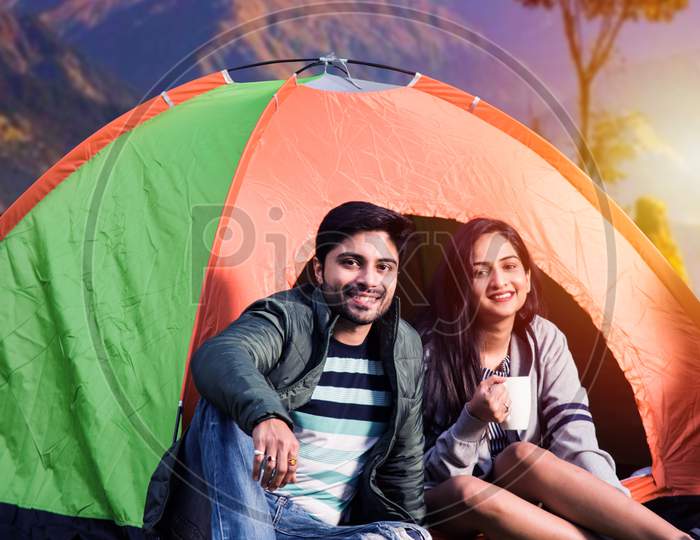 Indian Asian Young Couple, Camping And Having Tea While Sitting By Tent At Campsite