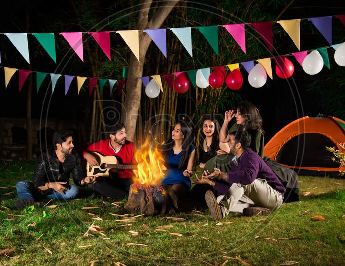Indian Asian Young Friends Playing Music And Enjoying Bonfire Or Campfire In The Night