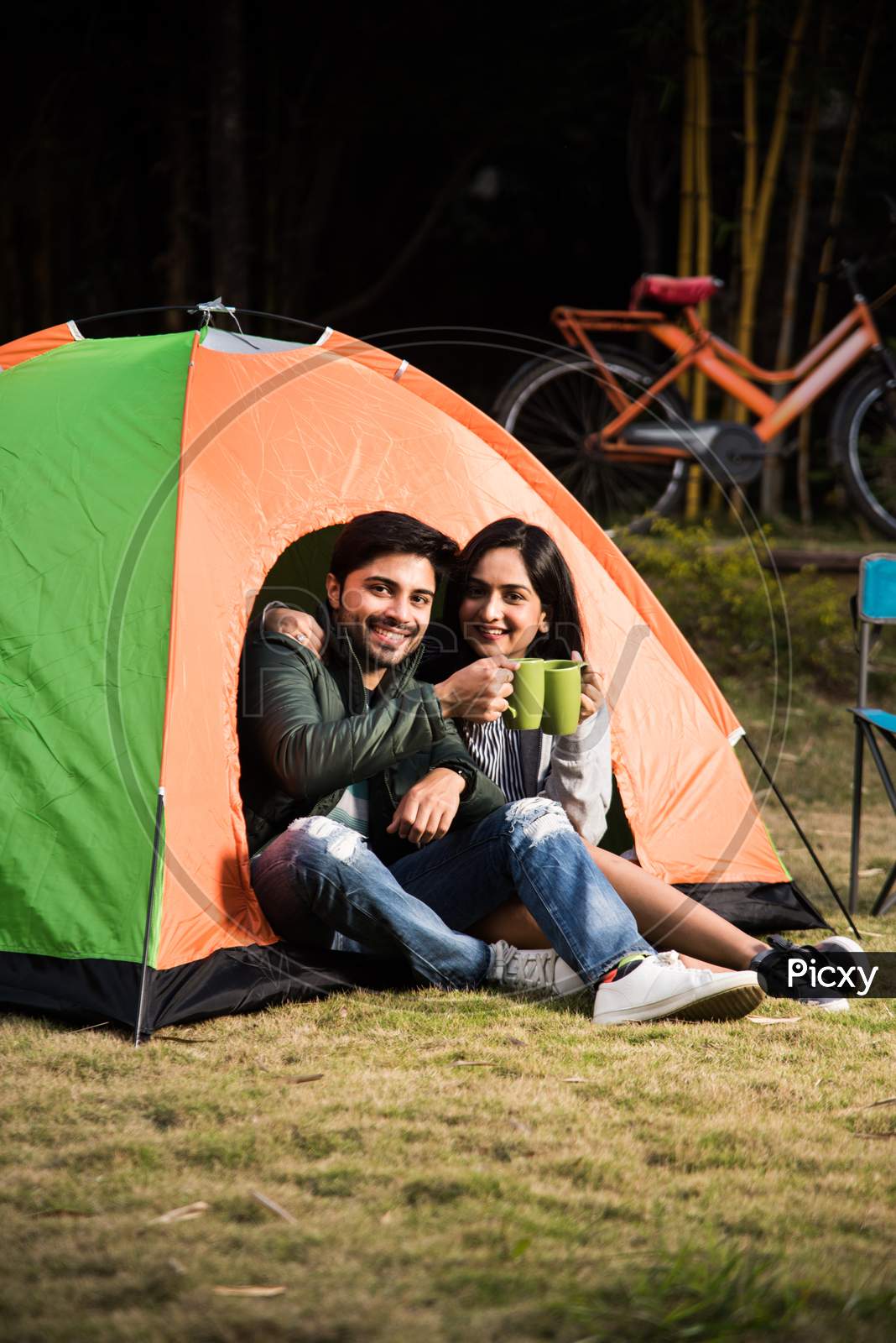 Indian Asian Young Couple, Camping And Having Tea While Sitting By Tent At Campsite