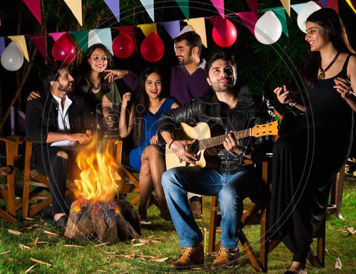 Indian Asian Young Friends Playing Music And Enjoying Bonfire Or Campfire In The Night