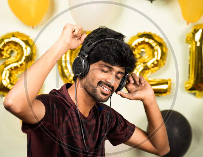 Young Man Enjoying By Listining Music On Headset Over 2021 New Year Decorated Background - Concept Of Solo New Year Partying Or Celebration Due To Coronavirus Pandemic.