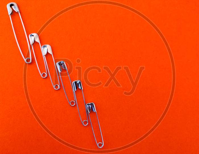 Safety Pins Are Arranged Like Taller To Smaller. Isolated On Orange Background,