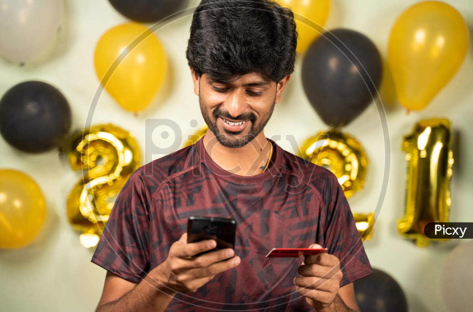 Young Man Busy In Purchasing Or Doing Online Payment On Mobile During Holiday Seasonal Sale On 2021 New Year Decorated Background - Concept Of Ecommerce, Technology, Internet For Shopping On Mobile.