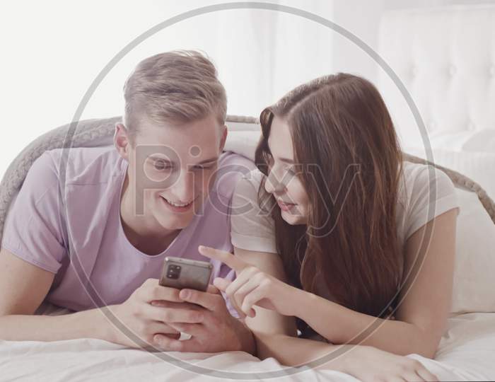 Couple Using Phone In Bed. Couple Shopping With Phone In Bed. Fun Shopping Online. Couple In Bed. Friends, Couple, Lovers Concept. Shot On Red
