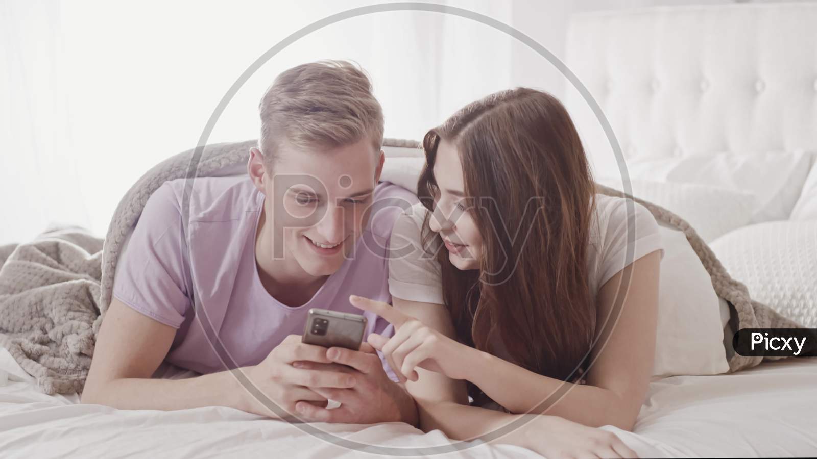 Couple Using Phone In Bed. Couple Shopping With Phone In Bed. Fun Shopping Online. Couple In Bed. Friends, Couple, Lovers Concept. Shot On Red