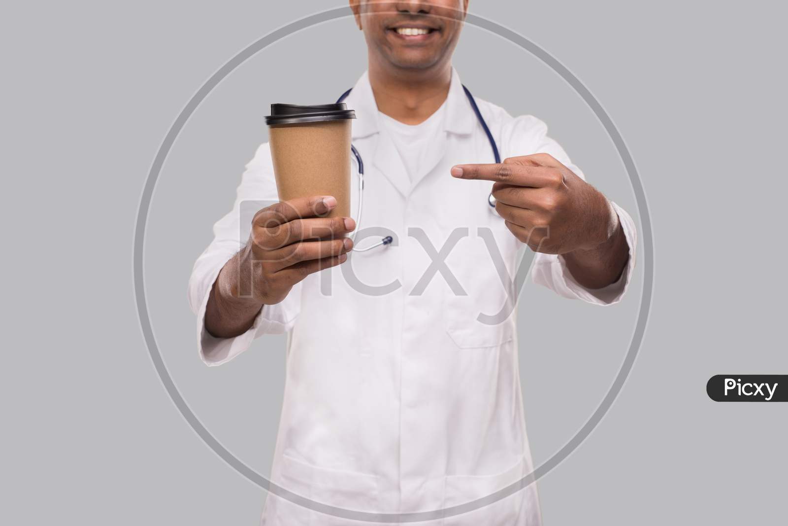 Doctor Pointing At Coffee Take Away Cup Smiling Close Up Isolated. Indian Doctor Holding Coffee To Go Cup.